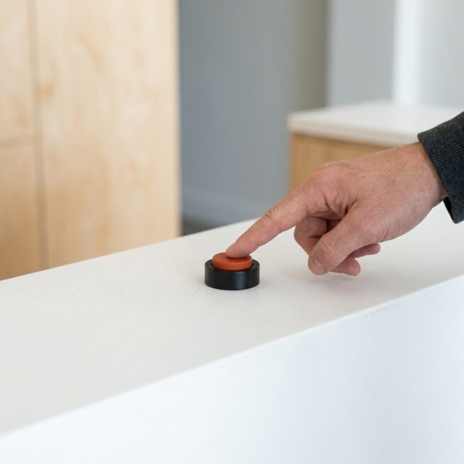 Hand drukt op een oranje oproepknop op een witte balie, als beeld voor het meten van een conversie