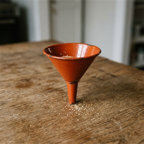 Oranje geëmailleerde trechter op een eiken tafel waar korrels doorheen vallen, als beeld voor leadgeneratie