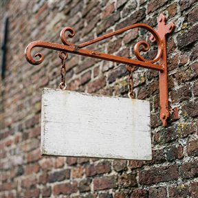 Blanco wit houten uithangbord aan een oranje smeedijzeren beugel tegen een bakstenen muur