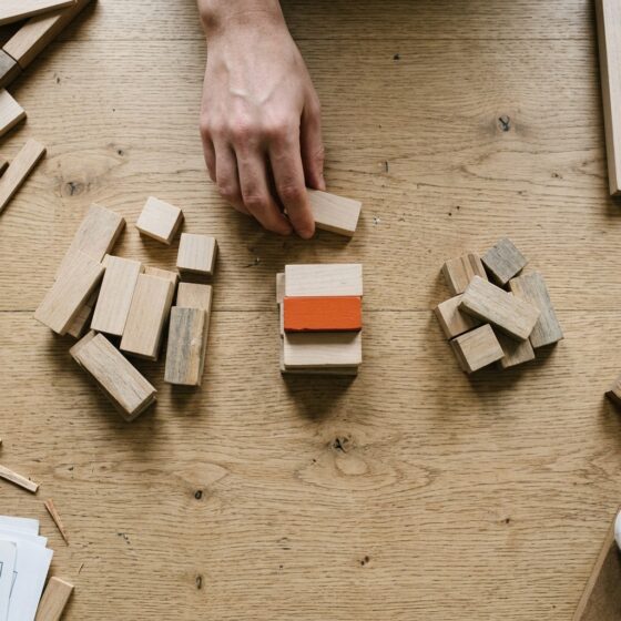 Hand sorteert houten blokken in drie stapels op een eiken tafel, waarbij één blok in de middelste stapel oranje is