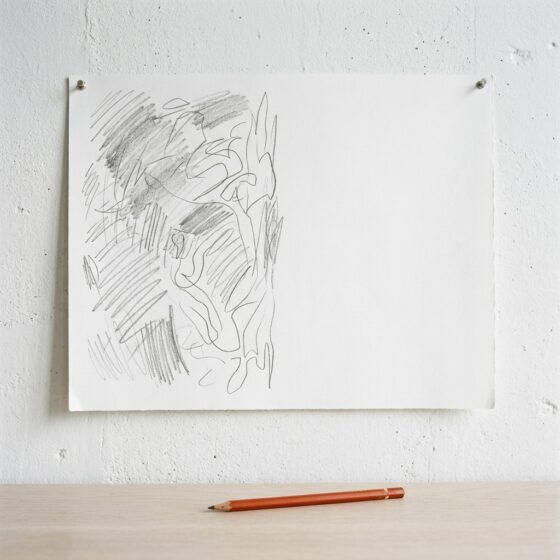 Wit vel papier aan een muur waarvan alleen de linkerhelft met potlood is ingevuld, met een oranje potlood eronder