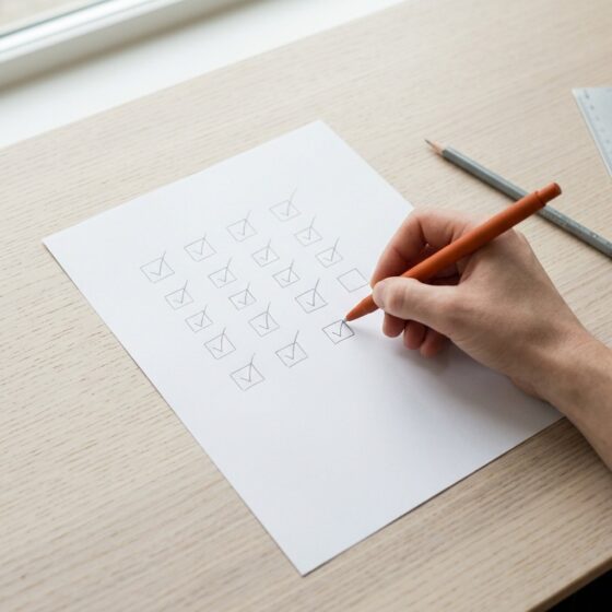 Hand zet met een oranje pen het laatste vinkje in een raster van getekende vinkvakjes op wit papier